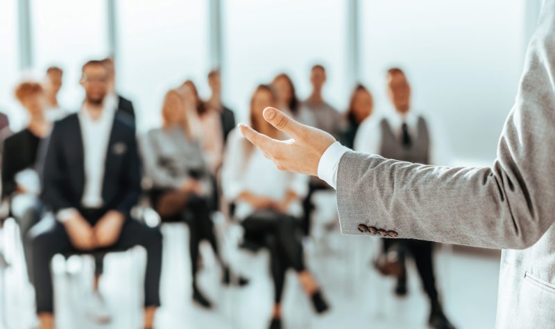 background image of a speaker standing in front of listeners in a conference room. photo with copy space