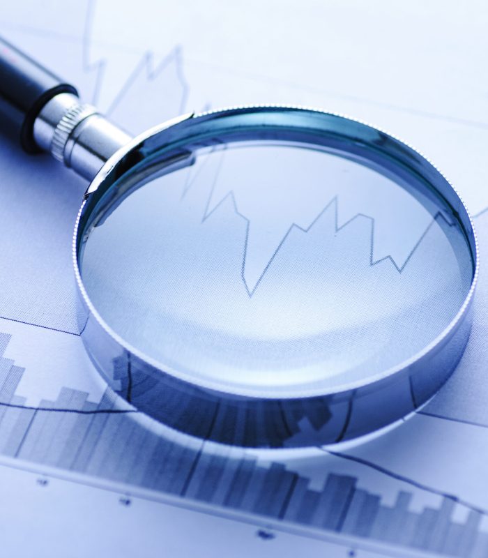 Magnifying glass with two fluctuating statistical business graphs in a concept of an audit, accounting analysis or market trends